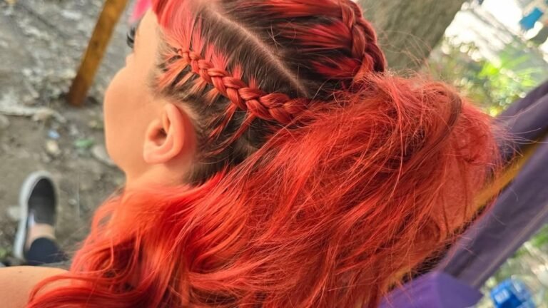 Woman with vivid red hair styled in twin braids wrapped around a high-volume teased ponytail