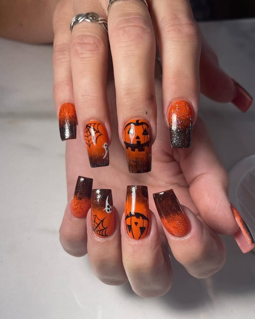 Coffin-shaped nails with a black-to-orange ombre, jack-o'-lantern face, ghost, and spiderweb Halloween nail art design
