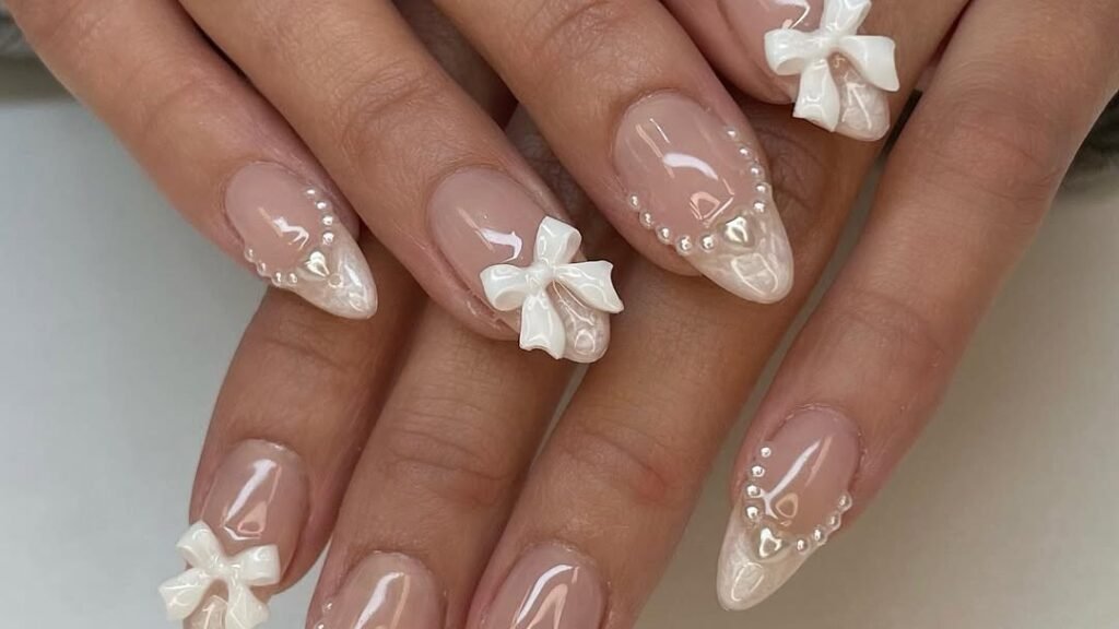 Nude bridal nails with 3D white bow details, pearl accents, and heart outlines for December wedding nail ideas