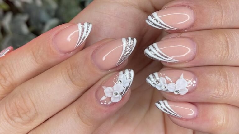 Close-up of two hands with short nude almond nails finished with white and silver glitter swoop tips, and two accent nails topped with raised white flowers and tiny clear crystals.