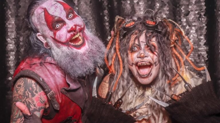 Two people in industrial steampunk Halloween makeup, one with red and white clown face paint and a gray beard, the other with smeared black and orange face paint and clawed gloves
