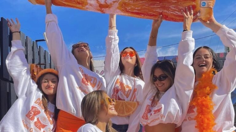 Group of friends in matching orange Halloween costumes holding a giant inflatable orange slice overhead