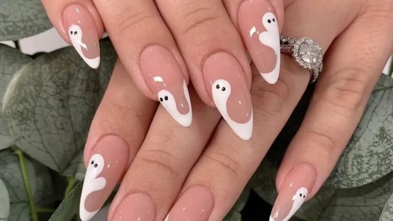 Long almond nails on a nude base with minimalist white ghost designs curling up from the tips, set against soft sage-green eucalyptus leaves