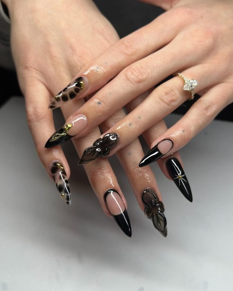 Black glossy French tip nails with sheer 3D flower petals and gold accents on an almond shape, styled as a Halloween wedding manicure with a diamond engagement ring