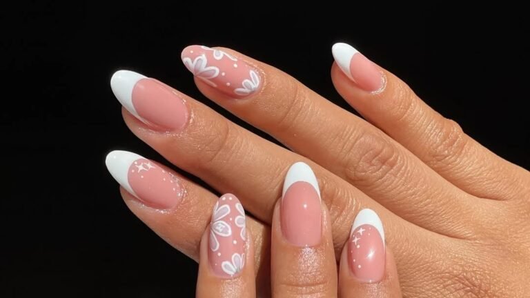 Almond nails with crisp white French tips over a sheer pink base, two accent nails hand-painted with white daisy-style flowers and tiny sparkles, shown on two hands against a solid black background.