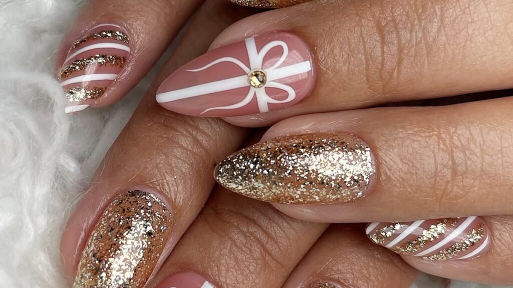 Gold glitter Christmas gel nails with a white gift bow design on almond-shaped tips