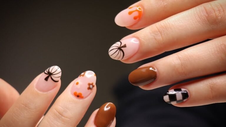 A hand with oval acrylic nails in warm fall tones, showing an orange pumpkin-drip nail, two matching bow-silhouette nails, tiny hand-painted florals, a solid glossy brown nail, and a black-and-white checkerboard nail