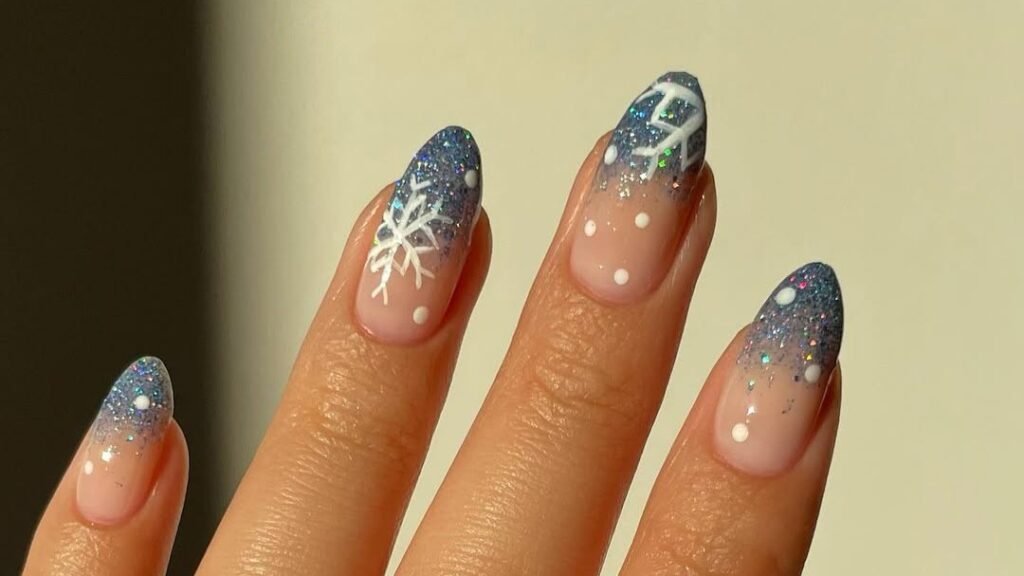 Icy blue glitter ombre nails with a hand-painted white snowflake accent nail, a winter nail idea