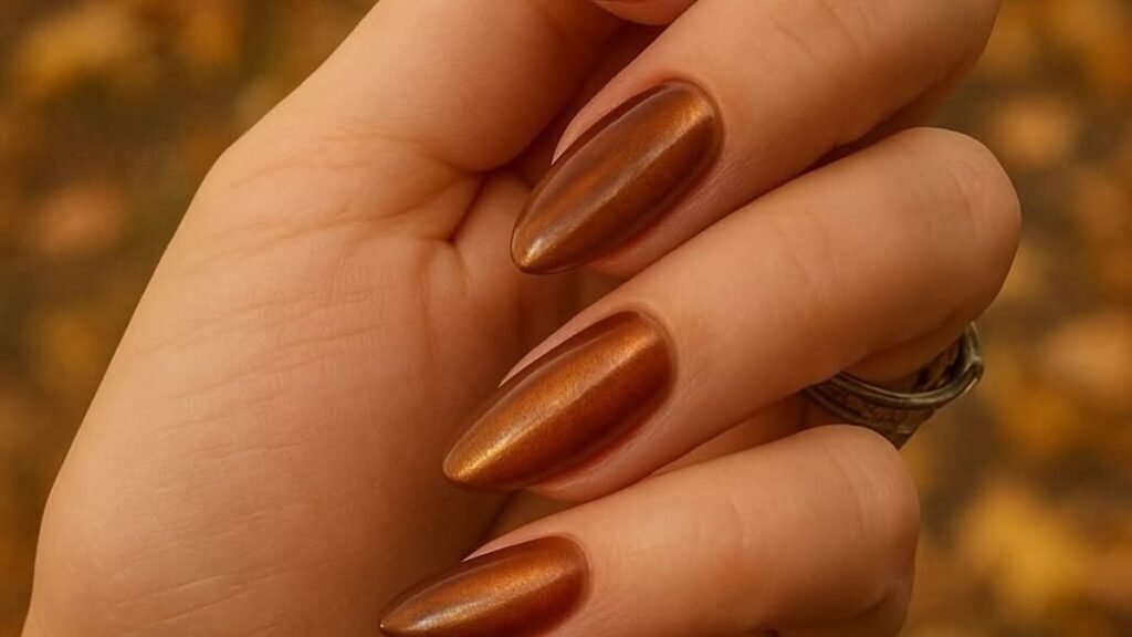 Copper chrome nail polish shimmering on almond-shaped nails, held in warm autumn light