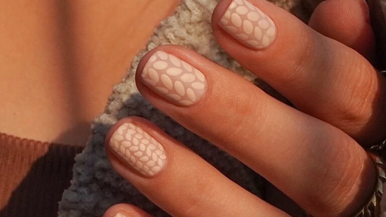 Nude nails with a raised leaf-stitch knit texture resting against a cream knit sweater sleeve