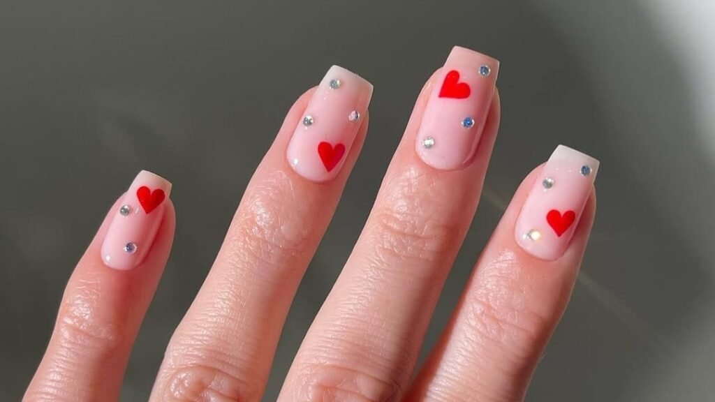Nude manicure with a single red heart and rhinestone accent on each nail for a February design