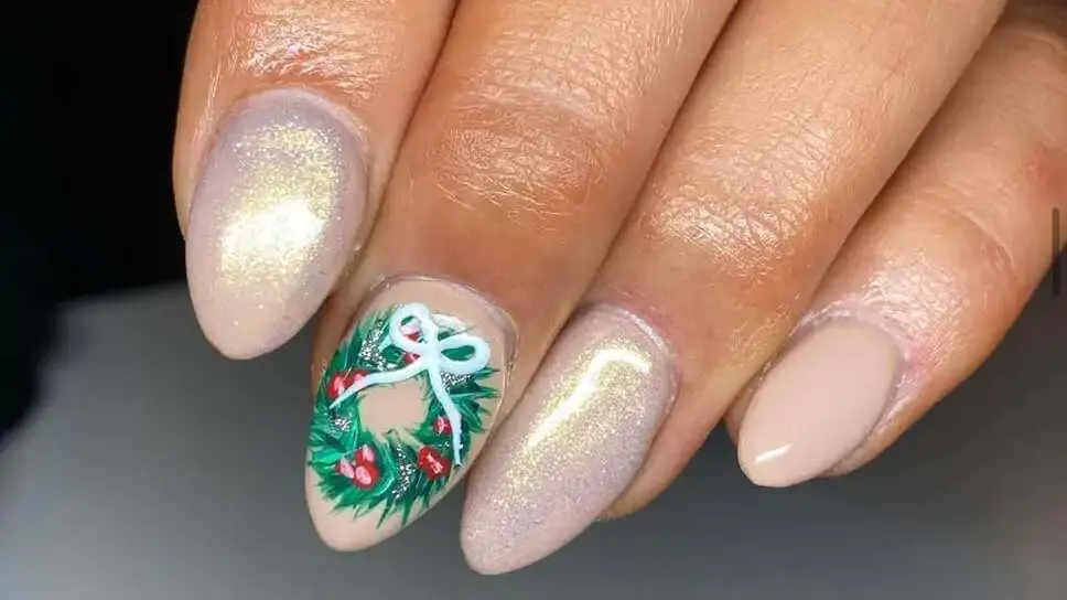 Detailed hand painted Christmas wreath nail with red berries and a white bow next to shimmering champagne gold nails
