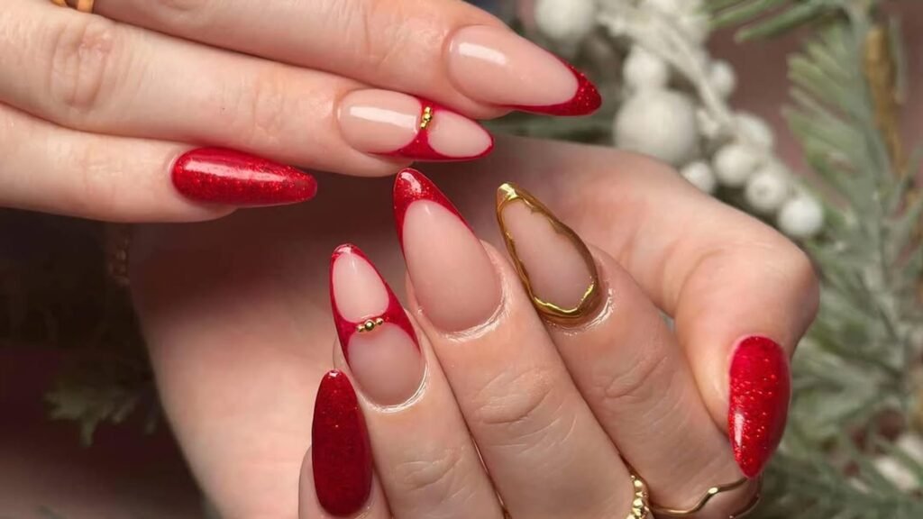 Almond nails with sheer nude bases, red French tips, a half-moon cuticle design with a small gold bead, one gold outline nail, and red glitter accent nails, shown with gold rings against frosted pine branches and white berries.