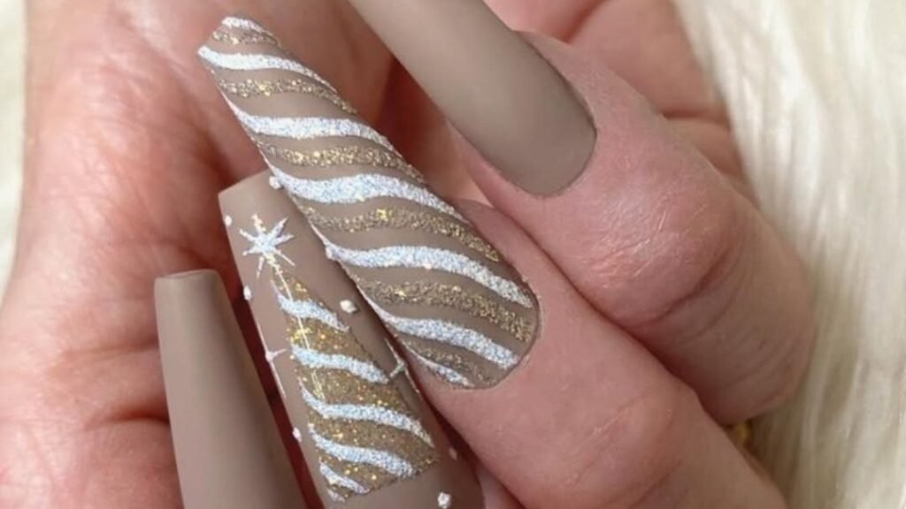 Matte mocha nude nails with a glitter Christmas tree accent nail and silver gold striped design, nude winter nail ideas