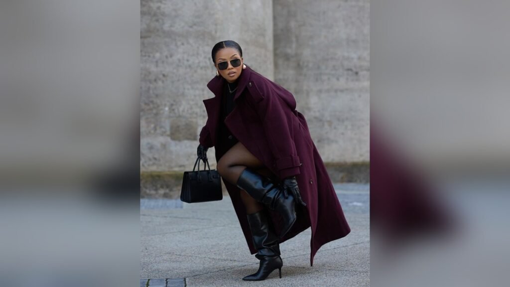 Plus size woman in a deep burgundy oversized coat and knee-high black boots walking confidently, styled for a winter outfit roundup