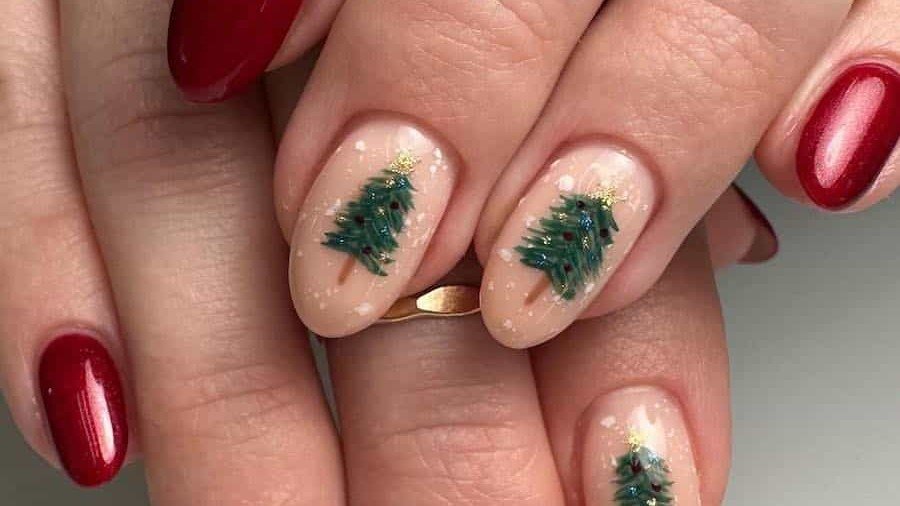 Nude nails with tiny hand-painted Christmas trees next to bold red nails, an example of Christmas nail ideas that skip the full paint job