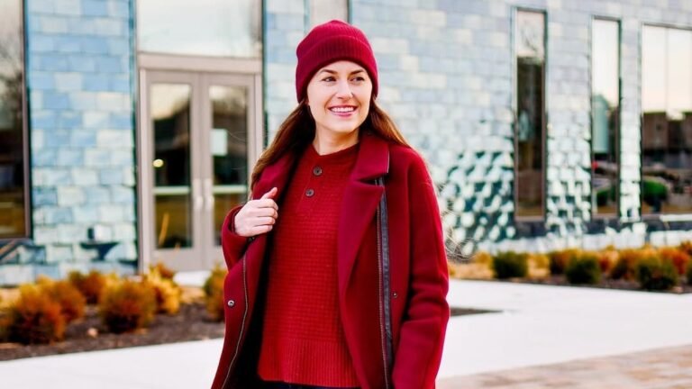 Woman in a red wool coat and matching beanie walking outdoors in a red sweater and jeans, a chic winter work outfit idea