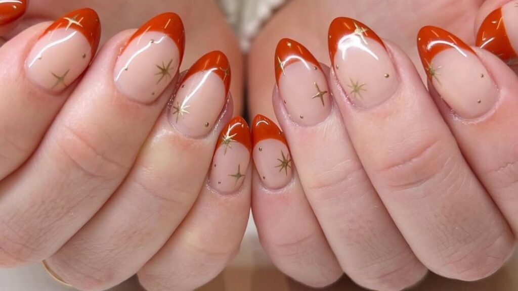 Rust orange French tip manicure with gold star nail art on warm neutral nails, ideal for a November nail look