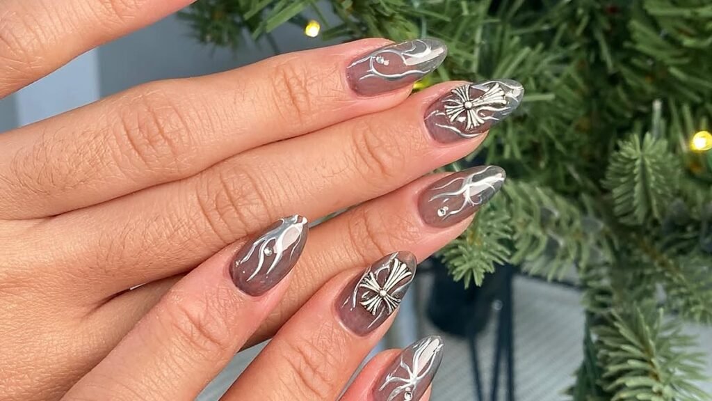 Almond nails in sheer smoky grey with raised silver chrome swirls and silver cross charms, held in front of a lit Christmas tree