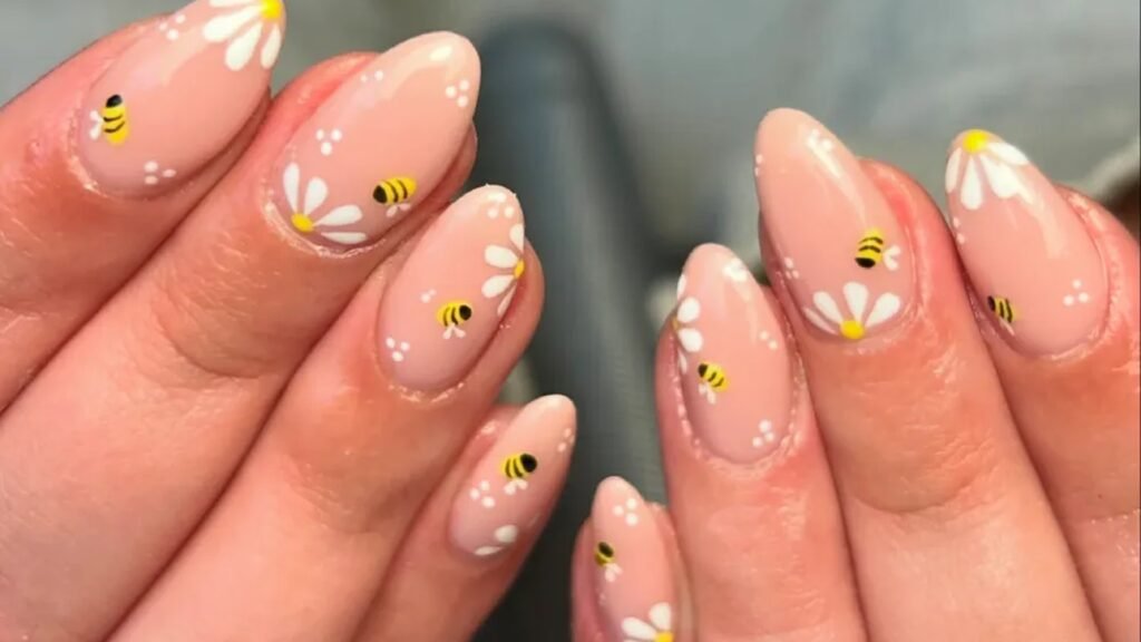 Bee and daisy nail art on short round nails, with tiny bumblebees and white daisies painted on a soft pink base