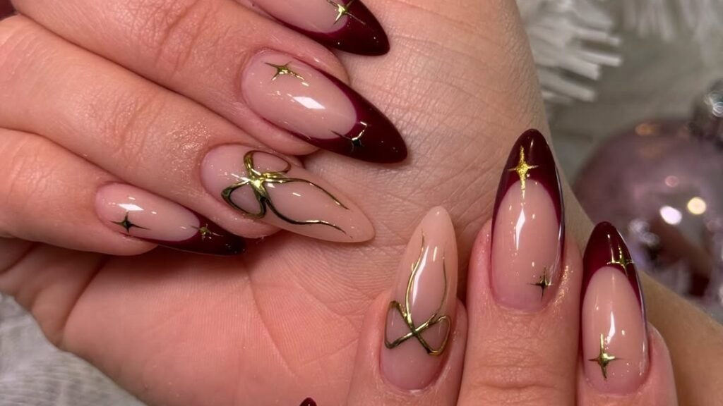 Wine red French tip nails with gold star and linework details on both hands, styled for winter
