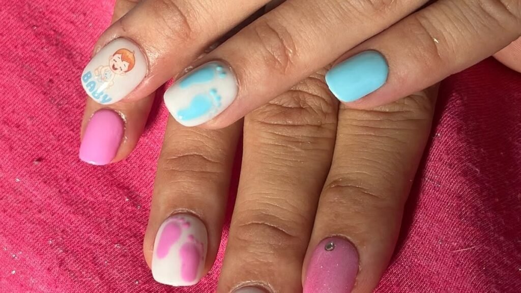 Pink and blue baby-themed nail art with tiny footprint designs, a cartoon baby illustration, and the word "BABY" on soft pastel nails