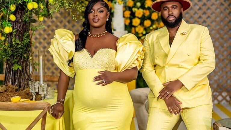 Pregnant woman in a yellow puff-sleeve gown and her partner in a matching yellow suit pose together at a lemon-themed baby shower with floral decor