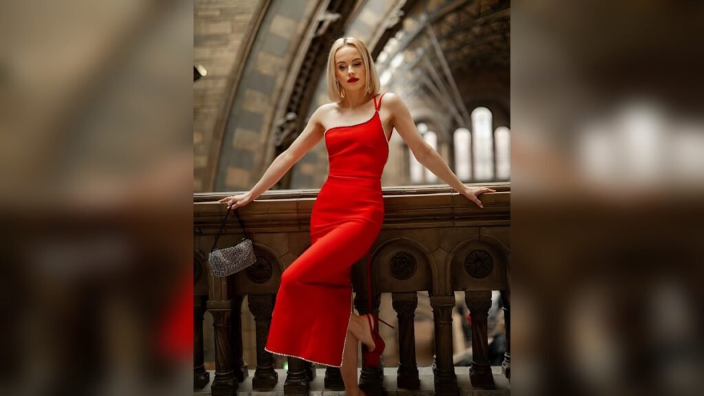 One-shoulder red midi dress with crystal trim and side slit, styled with a beaded clutch against dramatic arched architecture