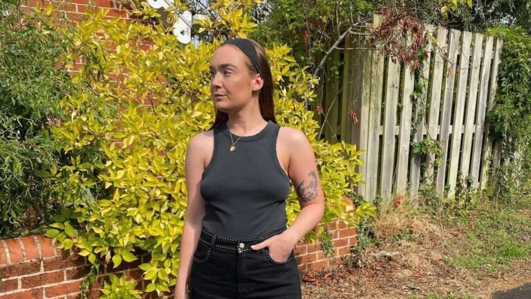 Woman in a black tank top and black maxi skirt with Birkenstock sandals against a bright green hedge