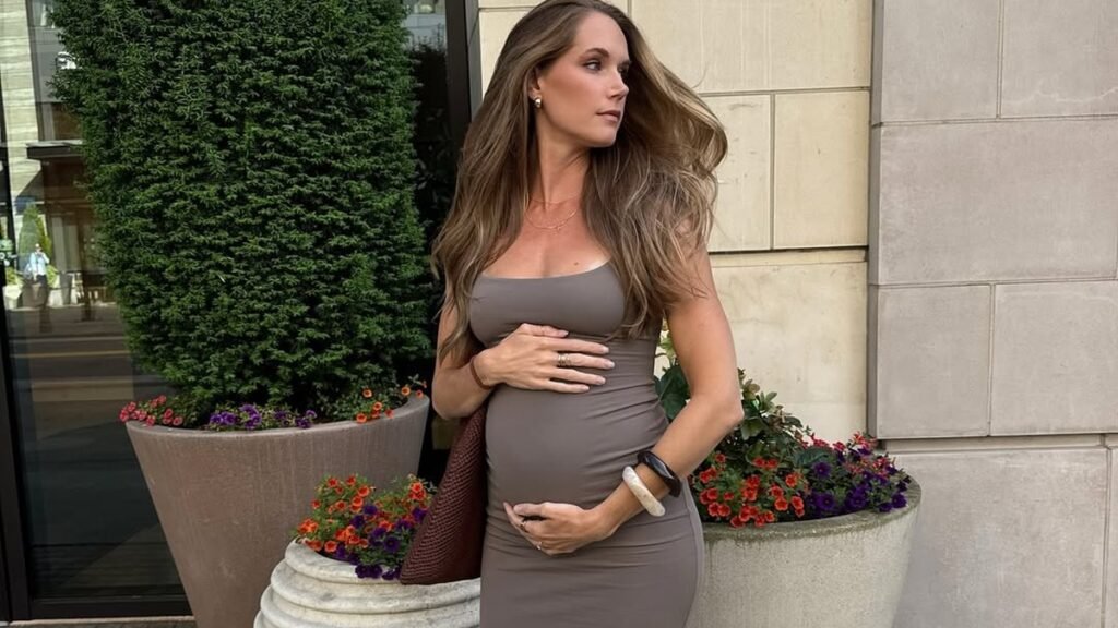 Pregnant woman in a cream trench coat over a taupe knit top and wide-leg pants, holding a brown suede bag, styled as a classy pregnancy outfit idea