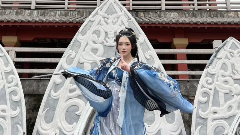 Woman in blue and silver hanfu with flared flowing sleeves posing mid-motion against carved stone archways in front of a traditional Chinese pagoda