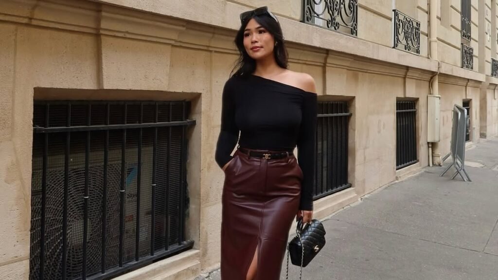 Woman wearing a burgundy leather midi skirt with front slit, black off-shoulder top, and knee-high boots, standing on a Paris street