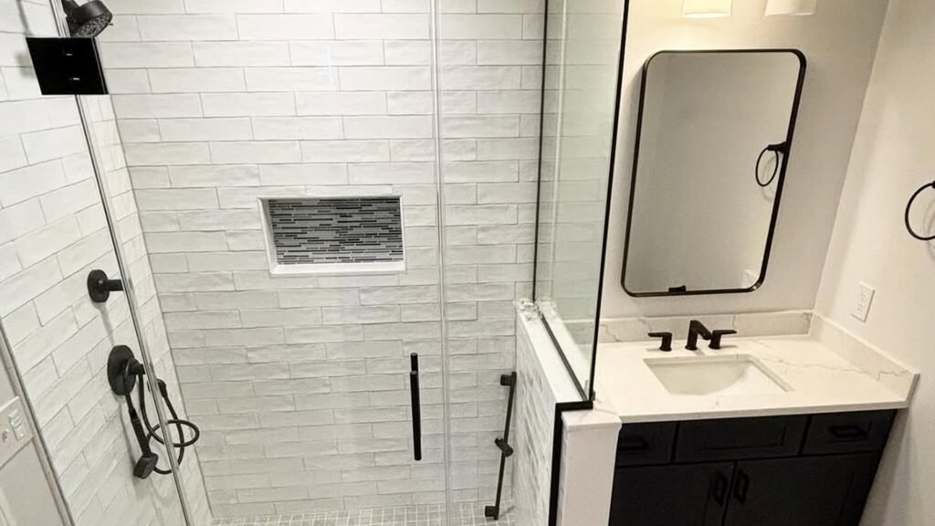Basement bathroom with a navy geometric-tile walk-in shower, black fixtures, and a white vanity with backlit mirror, no window in the room
