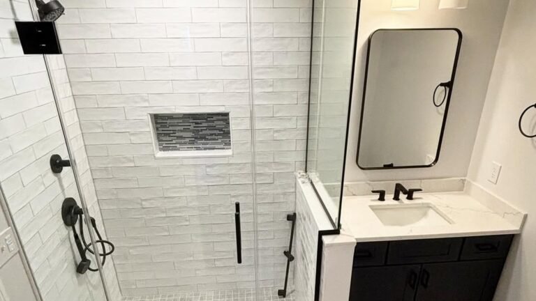 Basement bathroom with a navy geometric-tile walk-in shower, black fixtures, and a white vanity with backlit mirror, no window in the room