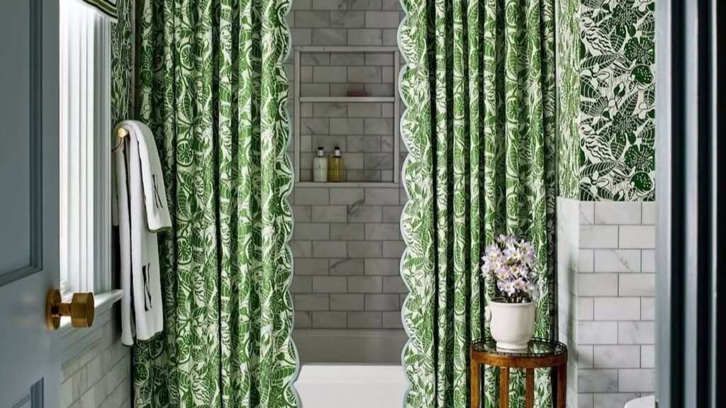 Green botanical print shower curtains with scalloped blue trim hanging from a ceiling-height valance beside a white marble tile tub alcove