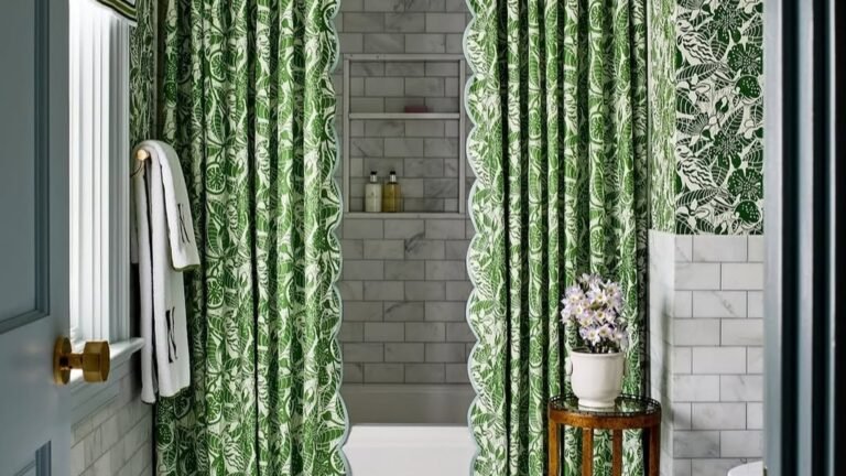 Green botanical print shower curtains with scalloped blue trim hanging from a ceiling-height valance beside a white marble tile tub alcove
