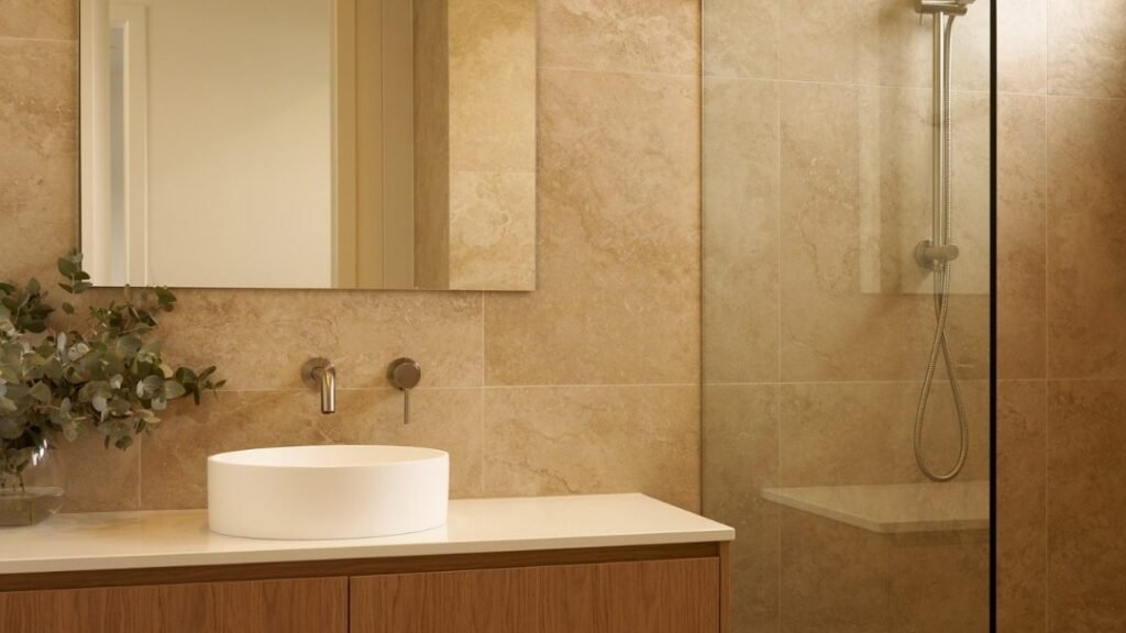 Warm beige bathroom with green tile accent, fluted wood vanity, and brass fixtures