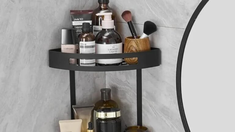 Matte black two-tier corner shelf mounted in a bathroom, holding toiletries and skincare bottles against light marble tile.