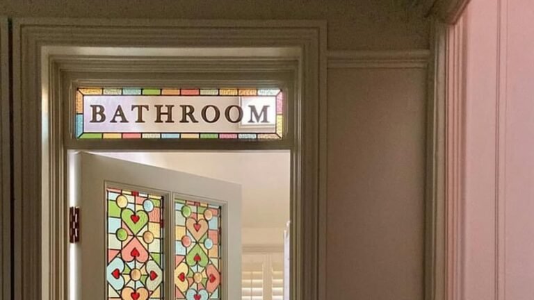 Antique stained glass bathroom door with a colorful heart pattern and a BATHROOM transom sign above the frame