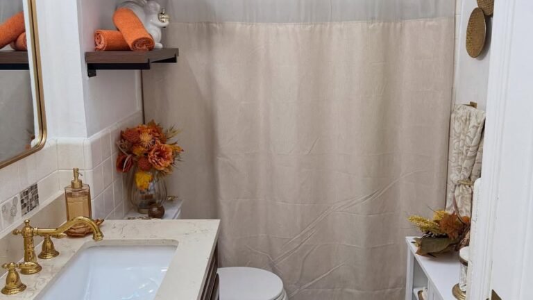 Bathroom vanity with double mirrors, brass faucets, and a small vase of warm orange fall flowers beside a lit candle