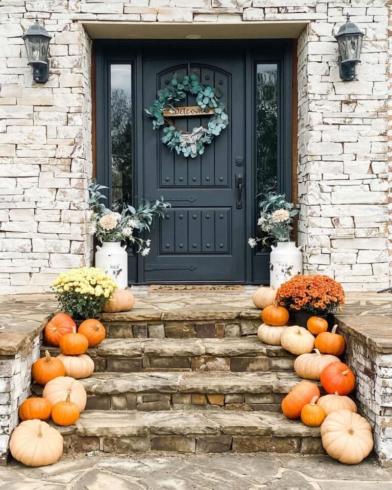High end fall decor porch with graduated neutral pumpkins on stone steps and a navy front door
