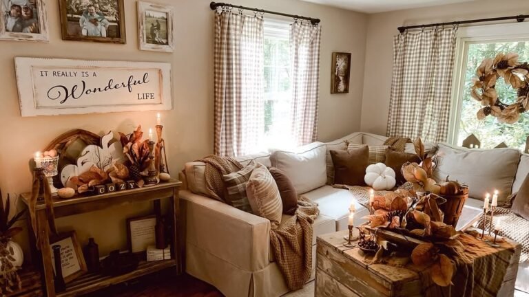 Cream sofa layered with beige throws and gingham curtains beside a candlelit centerpiece of dried leaves, one of 7 neutral fall decor ideas that feel rich not bare