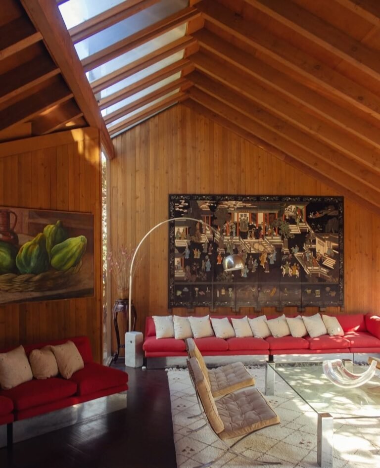 Red sofas in a mid century modern living room with a wood beam ceiling and paneled walls