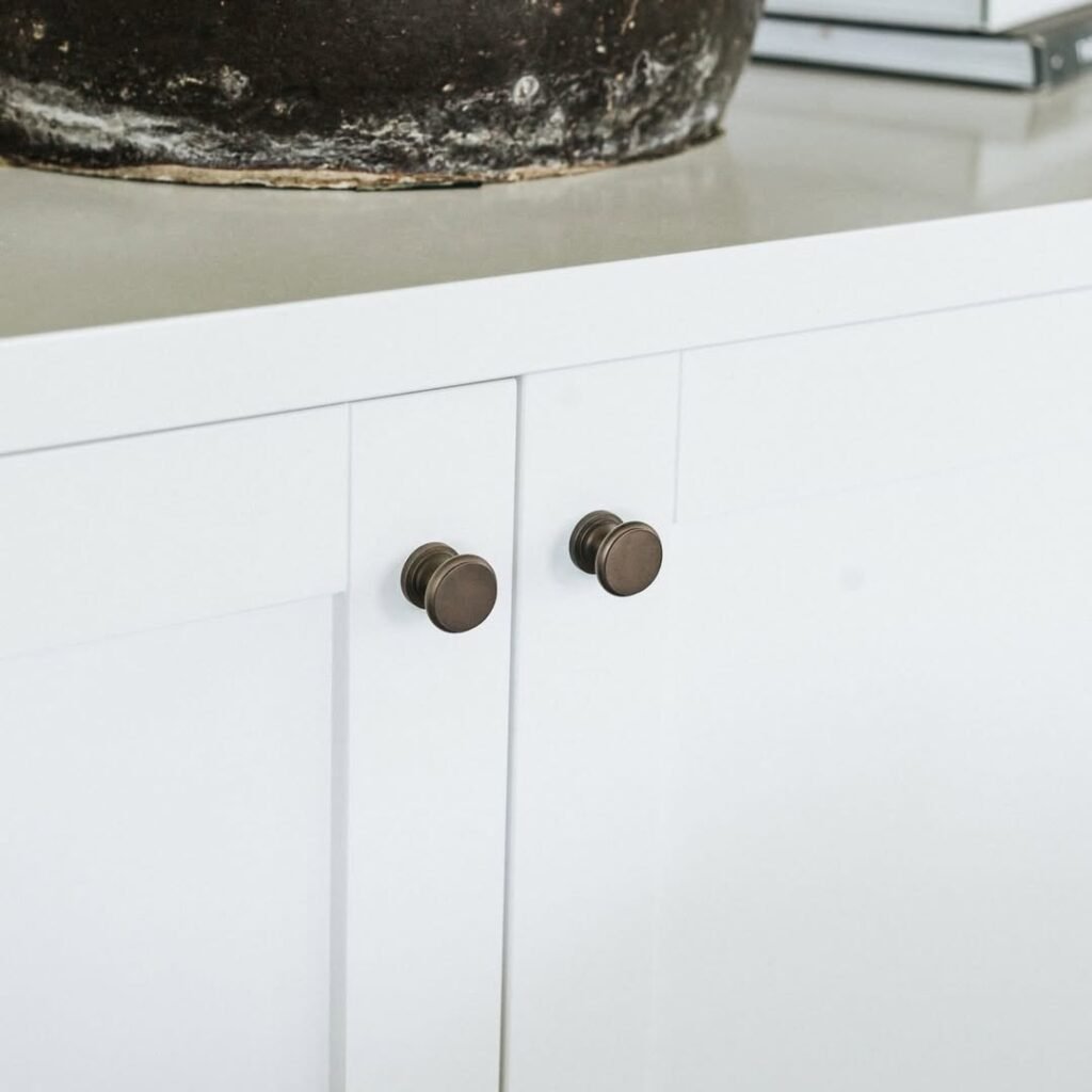 Two round aged bronze knobs centered on white Shaker cabinet doors, showing how dark knobs upgrade painted cabinets to look custom.