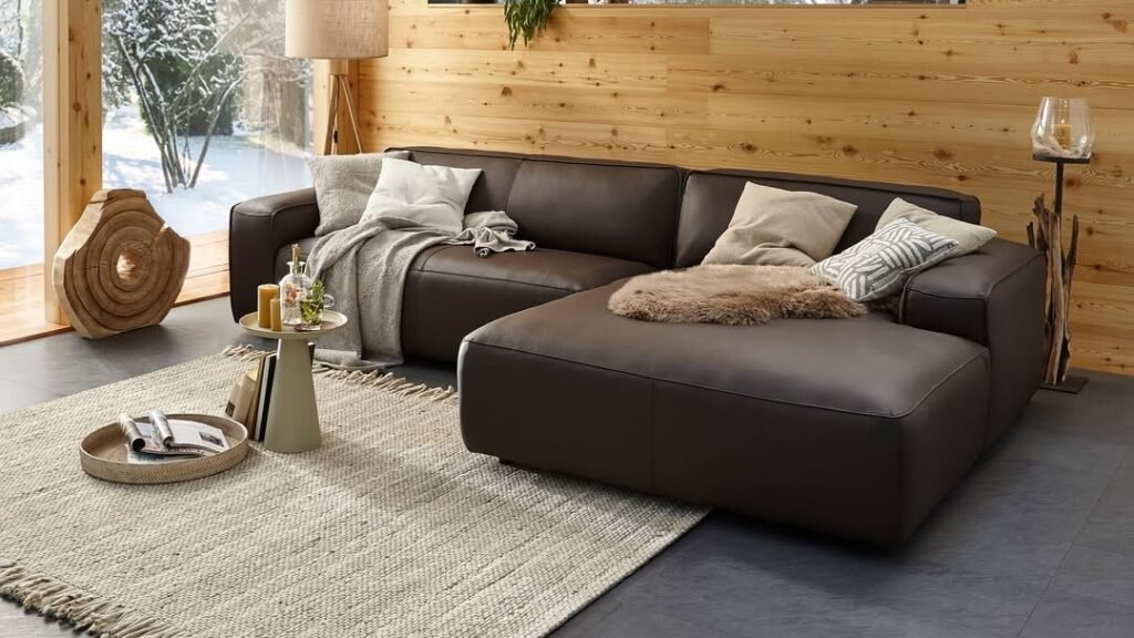 Modern living room with a chocolate brown leather sectional against a raw pine wall, warm wood tones and natural light replacing bold color