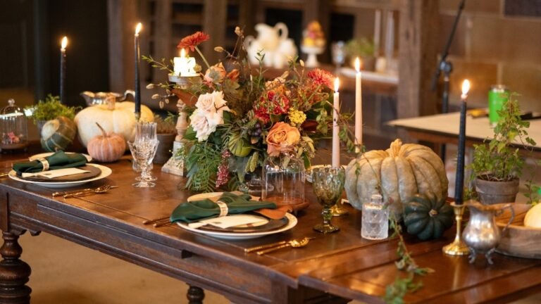 Rustic Thanksgiving decor with heirloom pumpkins, lit taper candles, green napkins, and a harvest floral centerpiece on a dark wood table in a barn