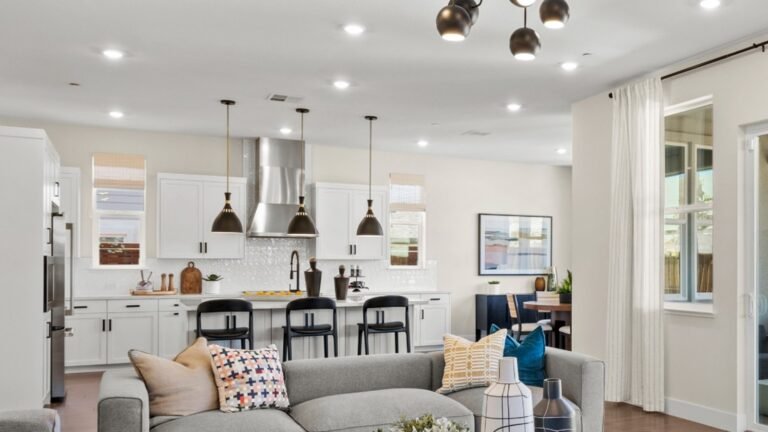 Open concept living room and kitchen with grey sectional sofa, wood coffee table, and white kitchen island in one unbroken sightline under a sputnik chandelier