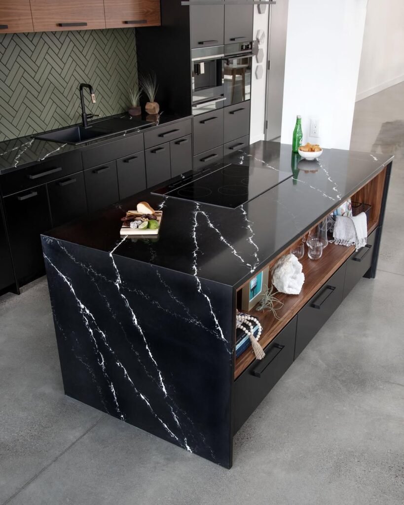 Black marble kitchen island with bold white veining and a waterfall edge, paired with walnut open shelving and olive herringbone tile