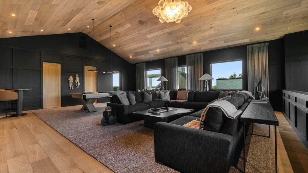 Black walled living room with warm oak vaulted ceiling, large sectional sofa, and wood coffee table