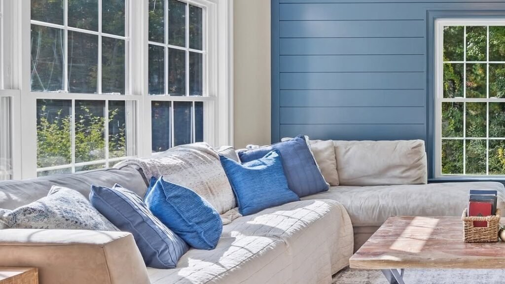 Living room with a bold blue shiplap accent wall, white trim windows, and a beige sofa styled with blue throw pillows